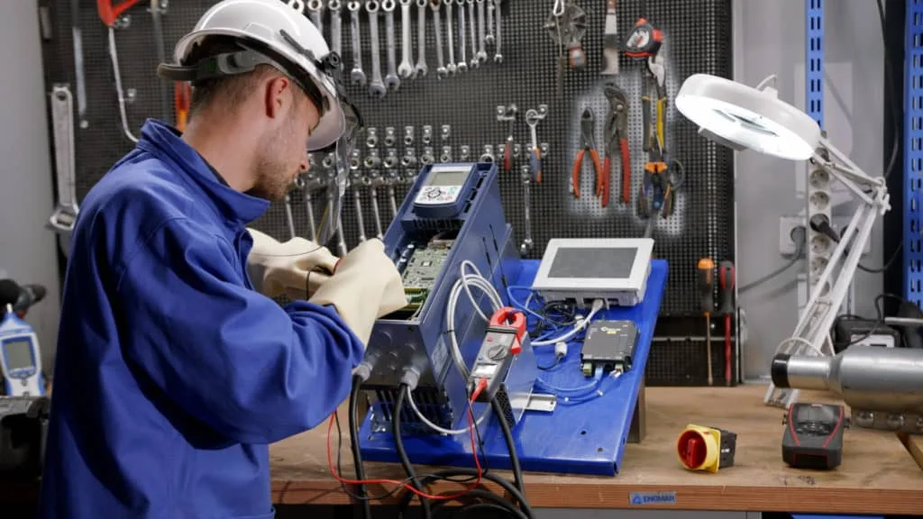 Technicien d’ENGMAR en blouse bleue contrôlant un boîtier électronique à l’établi