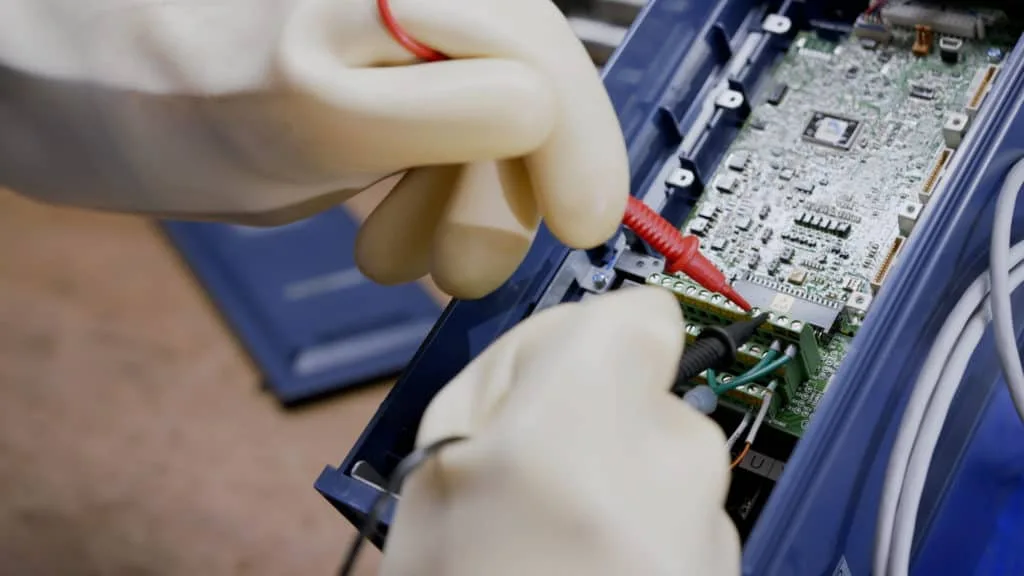 Mains gantées de blanc testant une carte électronique, atelier d’ENGMAR