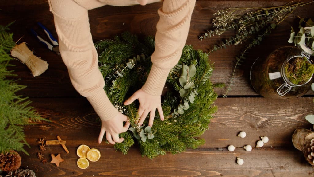 Mains assemblant une couronne de Noël en sapin et agrumes, tuto vidéo botanic