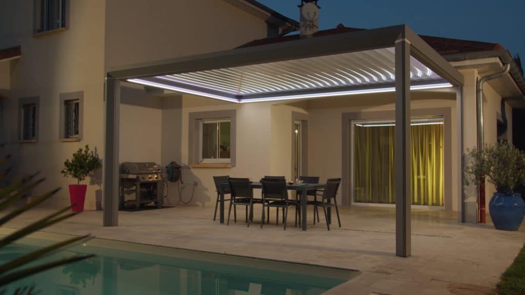 Pergola aluminium CEBEL éclairée à la tombée du jour au bord d’une piscine