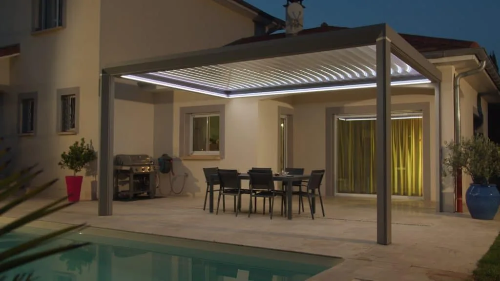 Pergola aluminium CEBEL éclairée à la tombée du jour au bord d’une piscine