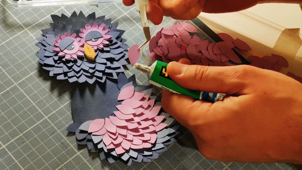 Mains qui collent un hibou en papier découpé en studio, fabrication des décors des spots Clémaflore