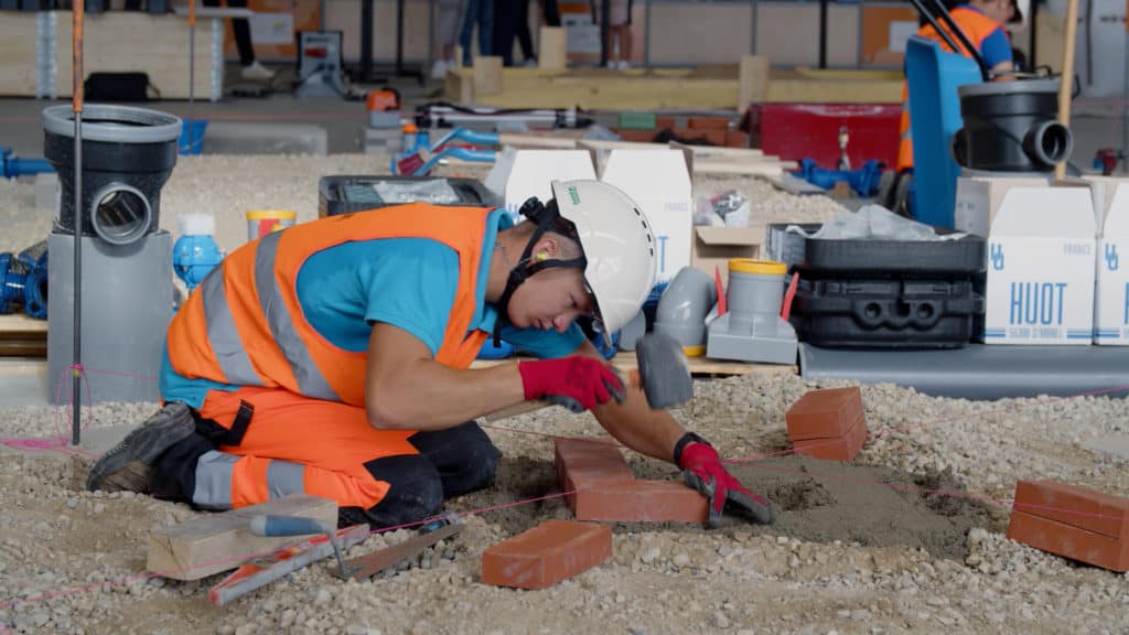 Compétiteur en maçonnerie, gilet orange et casque, qui pose des briques pendant WorldSkills France 2023
