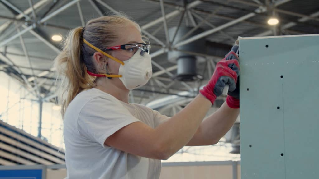 Compétitrice en plâtrerie, masque et lunettes, fixant une plaque pendant WorldSkills France 2023