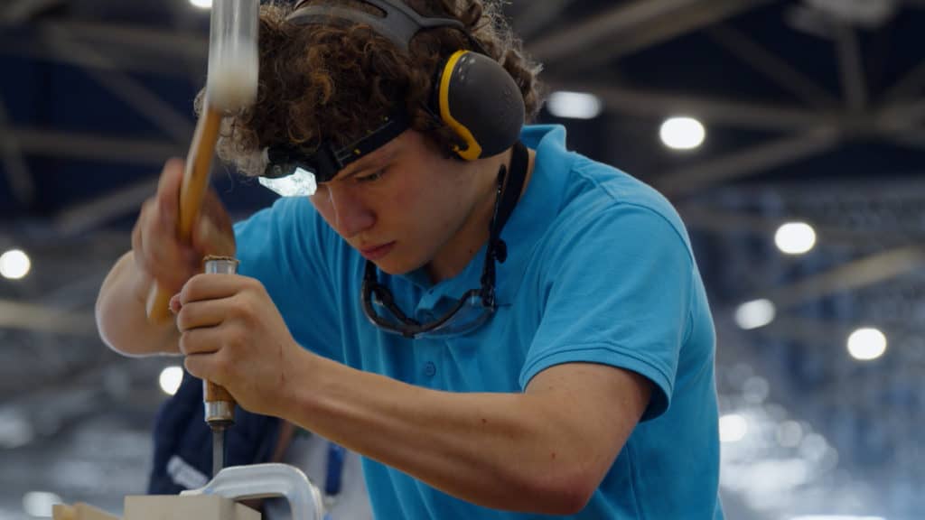 Compétiteur au casque antibruit, marteau levé sur son ouvrage, WorldSkills France 2023 à Eurexpo Lyon