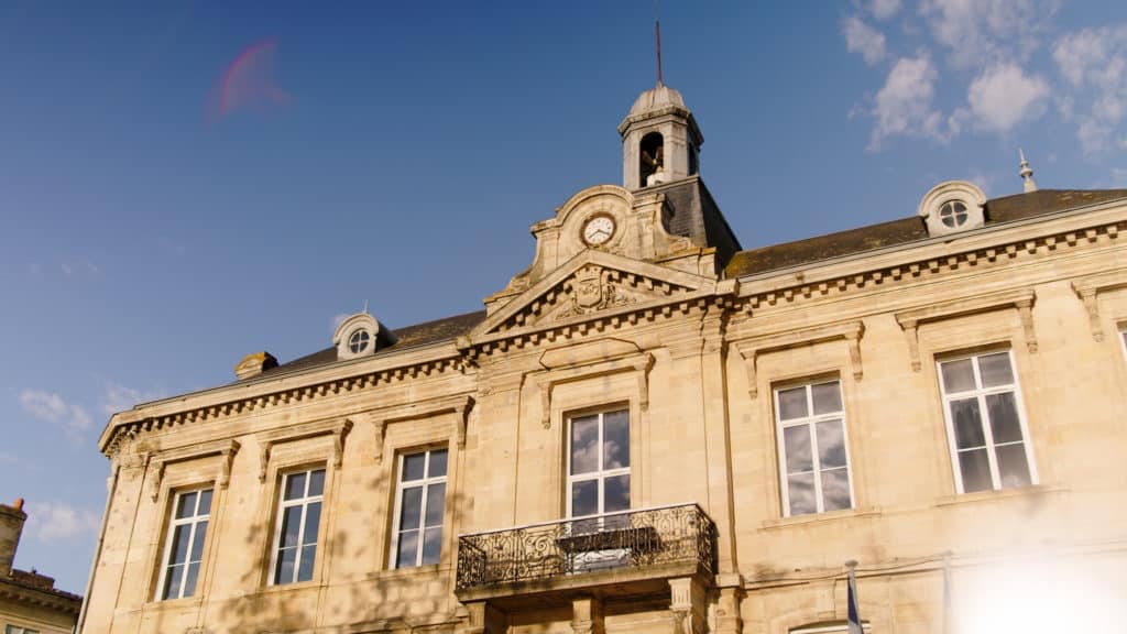 Façade en pierre blonde d’un édifice de Pauillac, horloge et clocheton, plan de contexte du film de marque