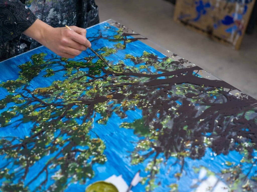 Clémentine Chalançon peignant le feuillage d’un arbre sur une toile bleue, portrait Allow.art