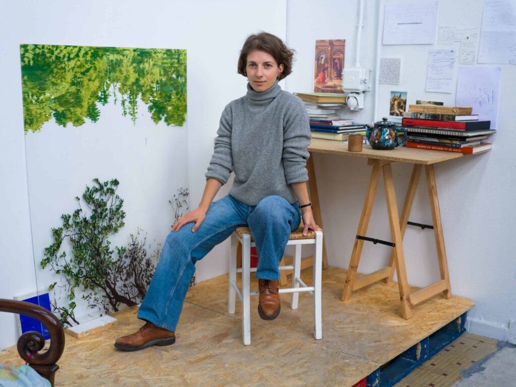 Clémentine Chalançon assise dans son atelier devant ses toiles de verdure, portrait Allow.art