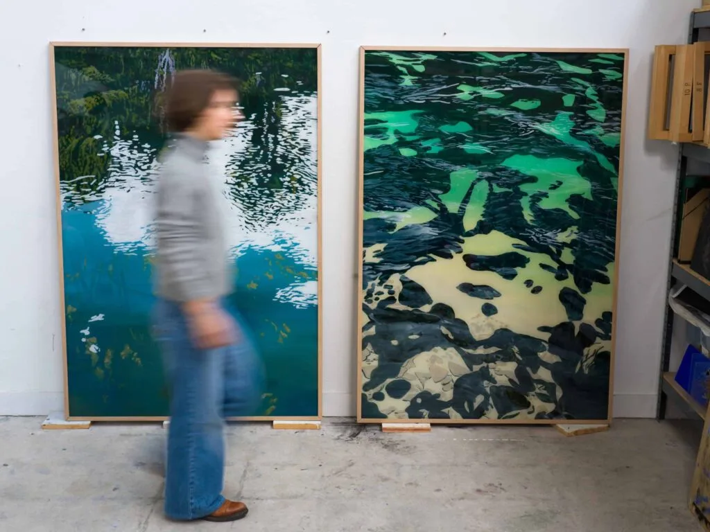 Clémentine Chalançon passant devant deux grandes toiles de reflets aquatiques dans son atelier, portrait Allow.art