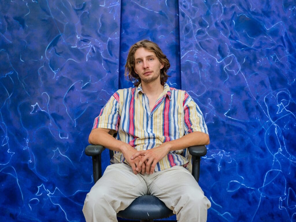 Lucas Zambon assis devant une toile bleue à l’encre, portrait Allow.art